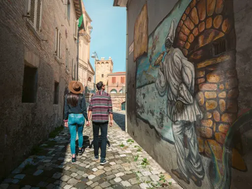 Coppia passeggia in un vicolo di Saludecio, ammirando un murale. Scopri cosa vedere in questo borgo incantevole.