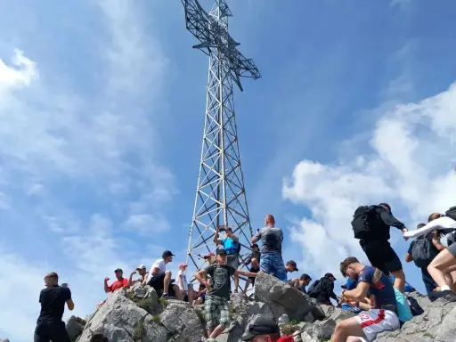 Grupa turystów na skalistym szczycie pod wysoką, metalową konstrukcją krzyża.