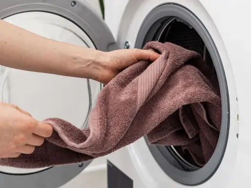 Manos colocando una toalla rosa en una lavadora. Aprende como lavar toallas para que queden suaves y esponjosas.