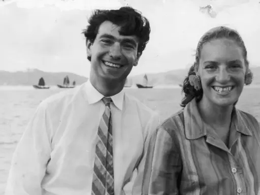 Angela Staude sorride con un uomo su una barca, con velieri sullo sfondo.