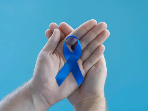 Dłonie trzymające niebieską wstążkę symbolizującą wsparcie dla mężczyzn. Warto poznać domowe sposoby na prostatę.
