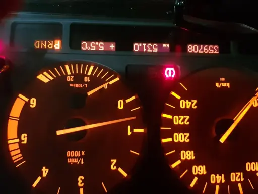 Czerwony wykrzyknik BMW świeci się na desce rozdzielczej, obok wskaźników prędkości i obrotów.