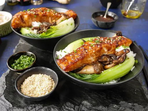 Två skålar med ris, bok choy, svamp och glaserad sous vide lax, toppad med sesamfrön och gräslök.
