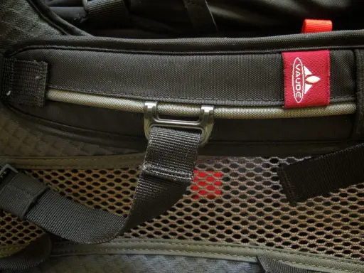 Czerwona metka z logo **Vaude** na czarnym plecaku. Firma Vaude to niemiecki producent sprzętu turystycznego.