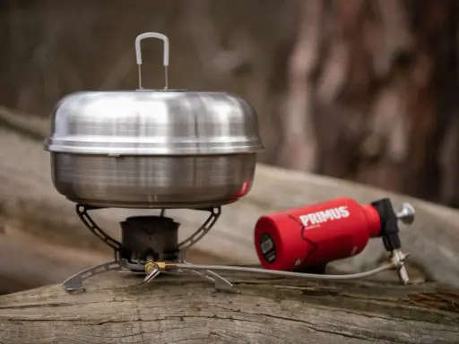 En primus kaffepanna på en campingkök med en röd gasbehållare. Perfekt för fika i naturen.