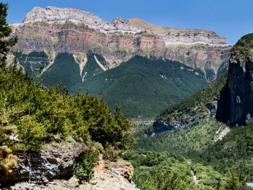 Paisaje de Ordesa y Monte Perdido con niños explorando senderos entre bosques frondosos y imponentes montañas.