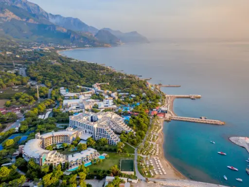Widok z lotu ptaka na Rixos Sungate, luksusowy kurort nad turkusowym morzem, otoczony zielenią i górami.