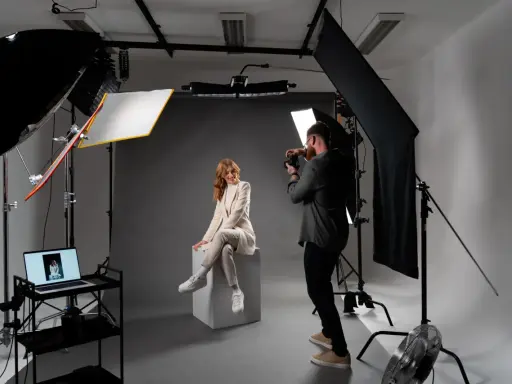 Profesjonalna fotografia studyjna: modelka w jasnym garniturze siedzi na kostce, fotograf robi zdjęcie.