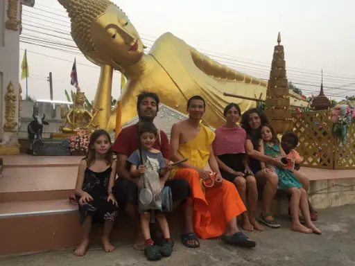 Familia disfrutando de un viaje a Asia con niños, sentados frente a una estatua dorada de Buda reclinado.