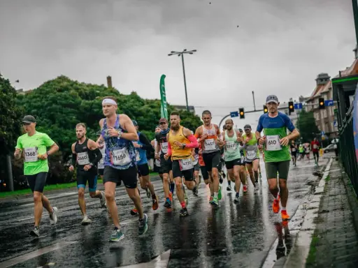 Uczestnicy maratonu biegną w deszczu po mokrej nawierzchni. Widać ich skupienie i determinację mimo niesprzyjającej pogody.