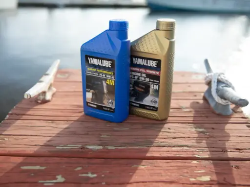Deux bidons d'huile Yamalube pour moteur 4 temps, l'un bleu (10W-30) et l'autre doré (5W-30), sur un ponton en bois.