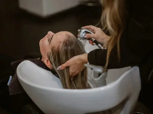 Una parrucchiera sciacqua i capelli di una cliente in un lavatesta, mostrando come lavare i capelli senza shampoo.