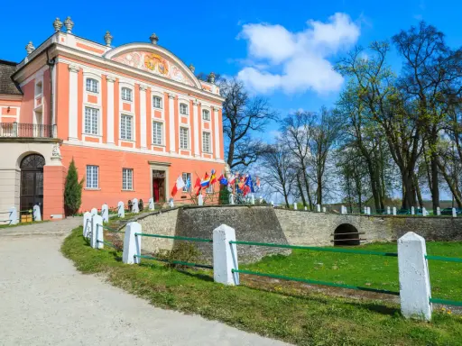 Pałac w Kurozwękach, z flagami narodowymi przed wejściem, zaprasza do odkrywania jego atrakcji.