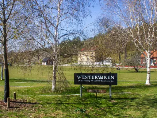 Vinterviken Stockholm, en grönskande park med träd och byggnader. En skylt visar "Winterviken - Festvåning - Café - Konferens".