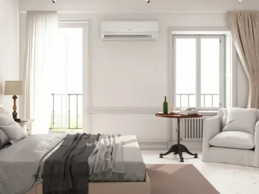 Un dormitorio luminoso con cama, armario de madera y aire acondicionado. La unidad de aire acondicionado está colocada estratégicamente en la pared, mostrando dónde colocar el aire acondicionado en un dormitorio para una climatización óptima.