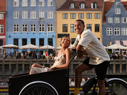 Ett par njuter av en romantisk weekend i Europa, cyklar längs en kanal med färgglada hus i bakgrunden.