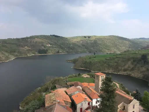 Villaggio pittoresco con tetti rossi e campanile affacciato su un lago serpeggiante, incastonato tra colline verdi vicino a Roanne, Francia.