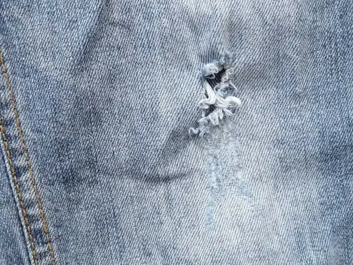 Jak zaszyć dziurę w spodniach dresowych? Widok z bliska na przetarty jeans z widocznym uszkodzeniem, które można naprawić.