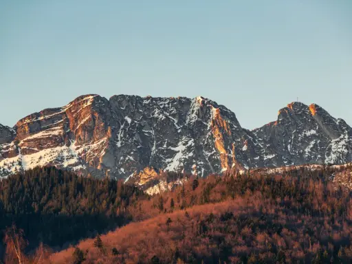 Skały Giewontu, ośnieżone i oświetlone słońcem, wznoszą się nad lasem. Choć trudno określić jaką wysokość ma Giewont, jego majestat robi wrażenie.