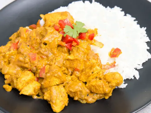 Pyszny kurczak curry z ryżem, udekorowany papryką i natką kolendry, podany na czarnym talerzu.