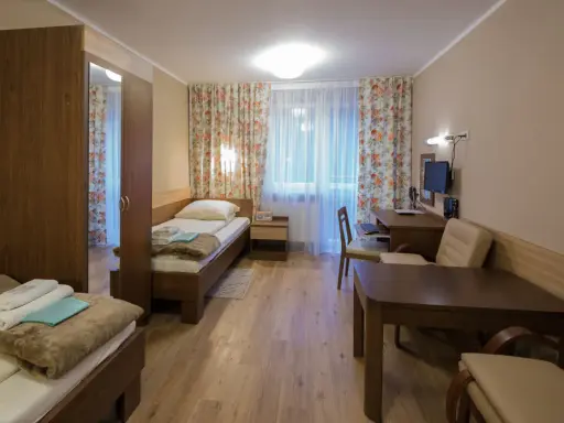 Pokój w sanatorium Włókniarz Busko-Zdrój: dwa łóżka, szafa, biurko z komputerem i stolik.