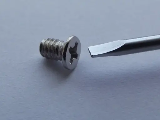 Tornillo metálico con cabeza de estrella y destornillador plano listo para ayudar a como quitar un tornillo pasado.