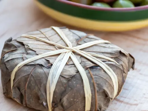 Un mets emballé dans des feuilles séchées, lié par des brins, évoquant les spécialités des Hautes-Alpes.