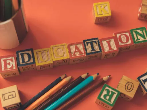 Klocki z literami tworzą napis EDUCATION. Obok leżą kredki i inne klocki, idealne do nauki tekstów po angielsku B2.