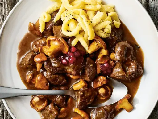 Herzhaftes Rehgulasch mit Rotwein, Pilzen und Preiselbeeren, serviert mit Spätzle. Ein köstliches Rehgulasch Rezept.