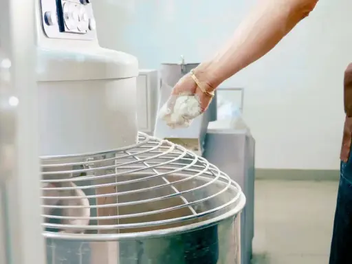 Main d'un boulanger ajoutant de la pâte à un pétrin, partie intégrante de l'entretien du matériel en cuisine.