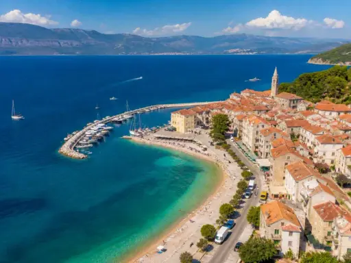 Malownicze miasteczko na wyspie Brač z portem pełnym łodzi, plażą i kamiennymi domami pod czerwonymi dachami.