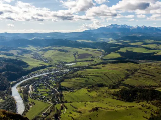 Widok na dolinę z rzeką i miasteczkiem, w oddali majaczą góry Tatry, które przypominają trzy korony. Wysokość widoku zapiera dech.