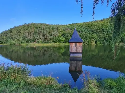 Holzhaus mit spitzem Dach, wie eine kleine Kirche im See, spiegelt sich im ruhigen Wasser.