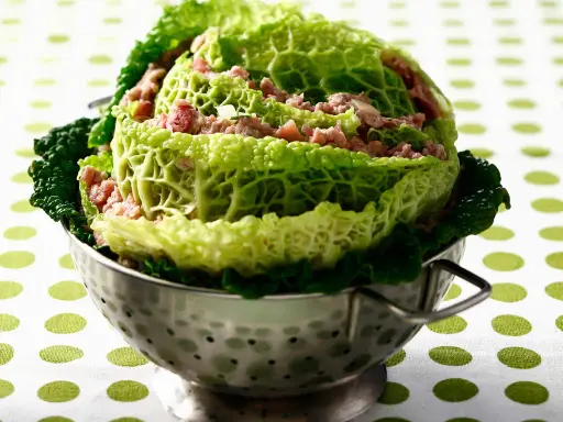 Un chou farci, recette traditionnelle, présenté dans une passoire en métal. Les feuilles de chou vert vif enrobent une garniture de viande hachée.