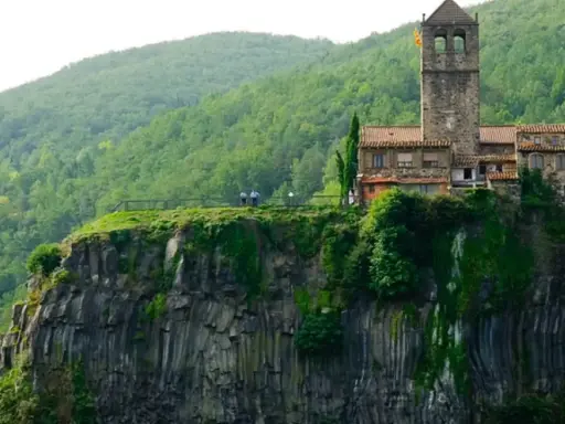 Castillo medieval en un acantilado, uno de los pueblos de Girona, rodeado de vegetación exuberante.