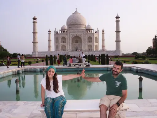 Pareja sonriente en la India, frente al Taj Mahal, con niños y visitantes al fondo.
