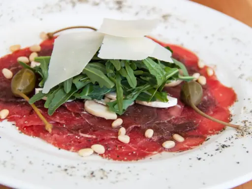 Delicato carpaccio di manzo con rucola, scaglie di parmigiano, pinoli, capperi e funghi champignon.