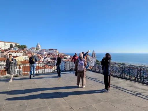 Blick vom Miradouro Portas do Sol auf Lissabons Dächer und das Meer. Touristen genießen die Aussicht.