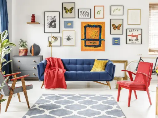 Salon w stylu eklektycznym: granatowa kanapa, czerwony fotel, dywan z geometrycznym wzorem i galeria obrazów na ścianie.