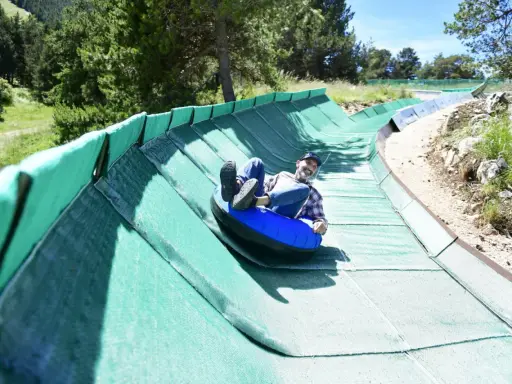 Un homme souriant dévale une piste verte en luge gonflable, profitant des activités Mont Ventoux.