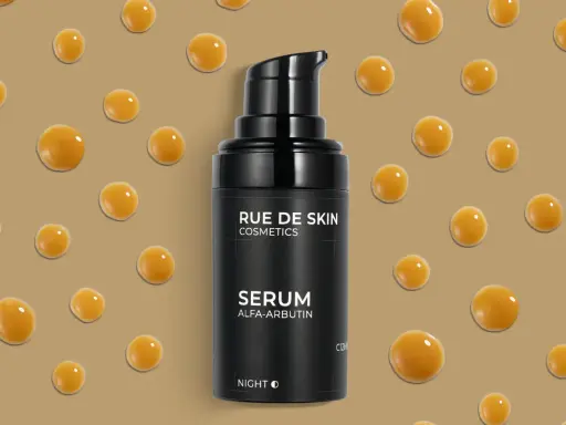 Serum z alfa-arbutyną od RUE DE SKIN. Krople serum unoszą się na beżowym tle, tworząc efekt kropli rosy.