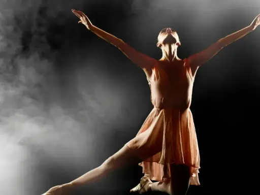 En ballerina i en ljusrosa klänning utför en graciös rörelse i klassisk balett, omgiven av dramatisk rök och ljus.