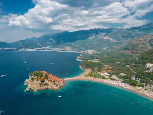 Malownicza wyspa Sveti Stefan, połączona z lądem piaszczystą mierzeją, otoczona turkusowym morzem i górami.