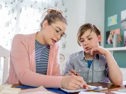 Junge Frau bietet Nachhilfe an. Sie erklärt einem Jungen konzentriert eine Aufgabe auf Papier.