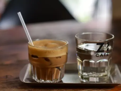 Kawa z lodem i słomką obok szklanki wody. Czy kawa jest moczopędna? Z's Cafe.