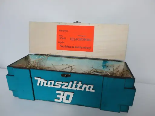 Otwarta, turkusowa skrzynka na 30 urodziny z napisem "Maszlitra 30". W środku sianko. Na wieczku etykieta "Najlepszy F(L)ACHOWIEC".