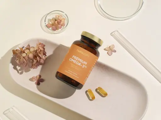 Butelka z suplementem omega 3 dla niemowląt, dwie kapsułki i suszone kwiaty na ceramicznej tacce.