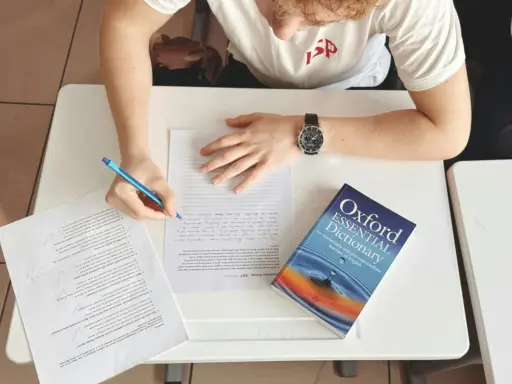 Uczeń pisze wypracowanie, a obok leży słownik "Oxford Essential Dictionary". Zastanawia się, co to jest "suffix" i jak go użyć.