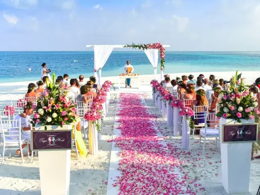 Plażowa ceremonia ślubna z różowymi płatkami kwiatów i widokiem na ocean. Idealne miejsce na ślub, które marzy się wielu parom.