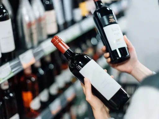 Manos sostienen botellas de vino tinto, eligiendo entre los vinos más vendidos en España.